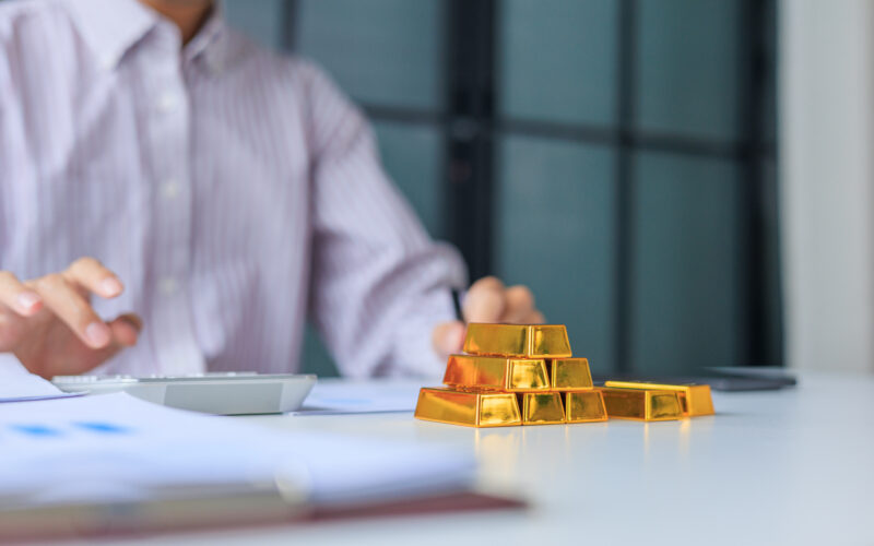 Selective focus on gold bars with background of hands using calculator for gold trading analysis. Concept for wealth management, asset protection, and financial planning.